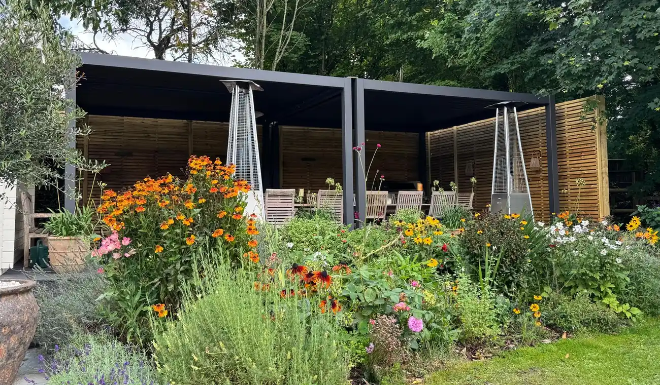 Anthracite louvred pergola with timber slatted privacy screens on two sides, deep flower border in front
