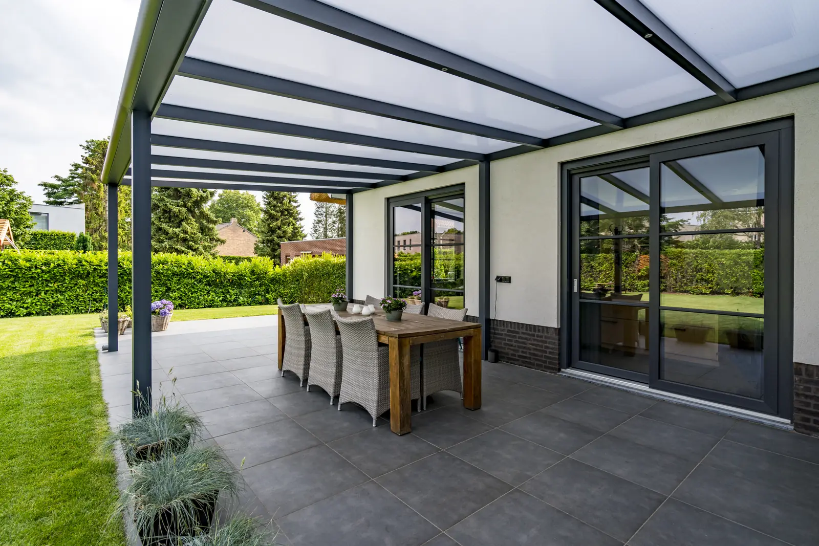 Glass veranda with an anthracite aluminium frame over a dining table, attached to a house