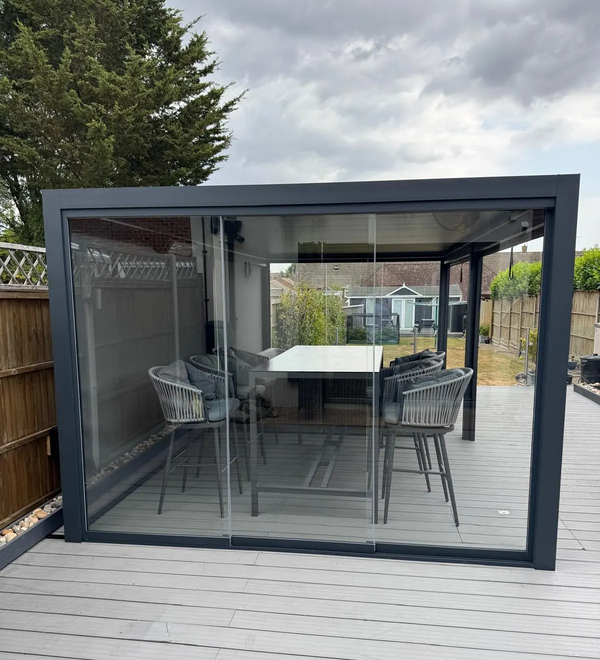 Morvelle pergola on composite decking, enclosed with sliding glass side panels around a dining set