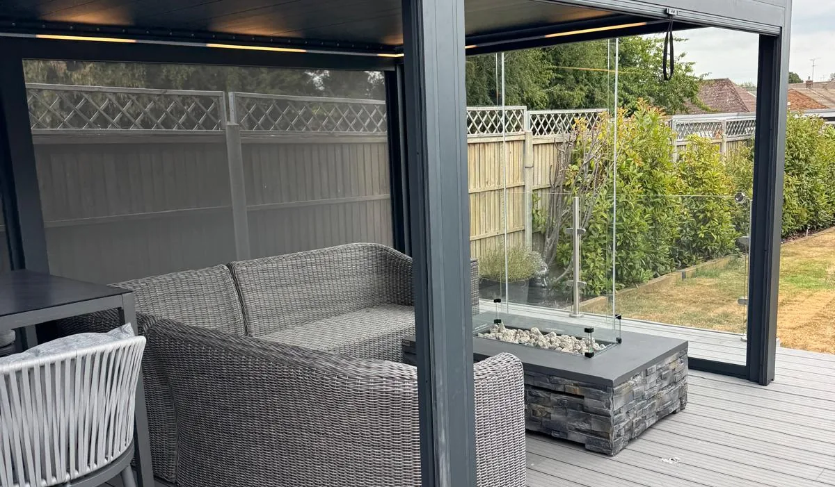 Morvelle pergola on composite decking with a corner sofa, gas fire table and lit roof underside