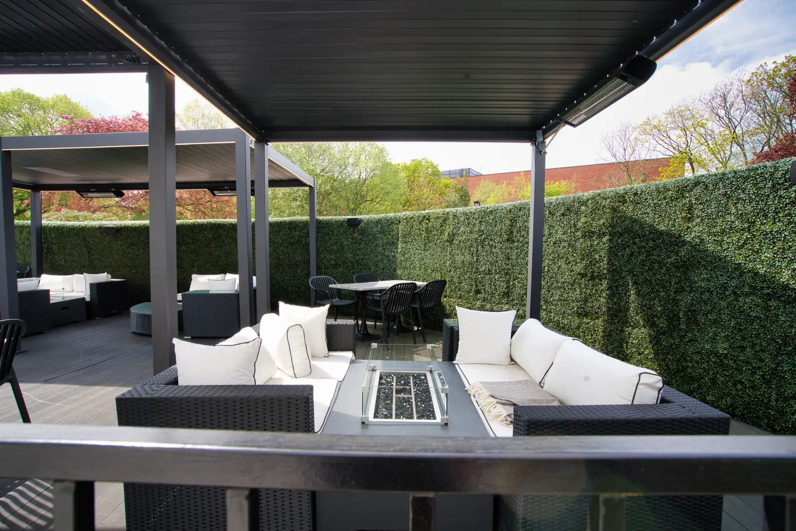 Infrared heaters and a fire table beneath louvred pergolas enclosed by tall hedges