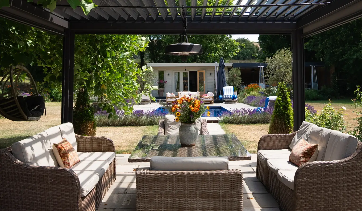 Louvred aluminium pergola over rattan lounge seating, with a pool and lawn beyond