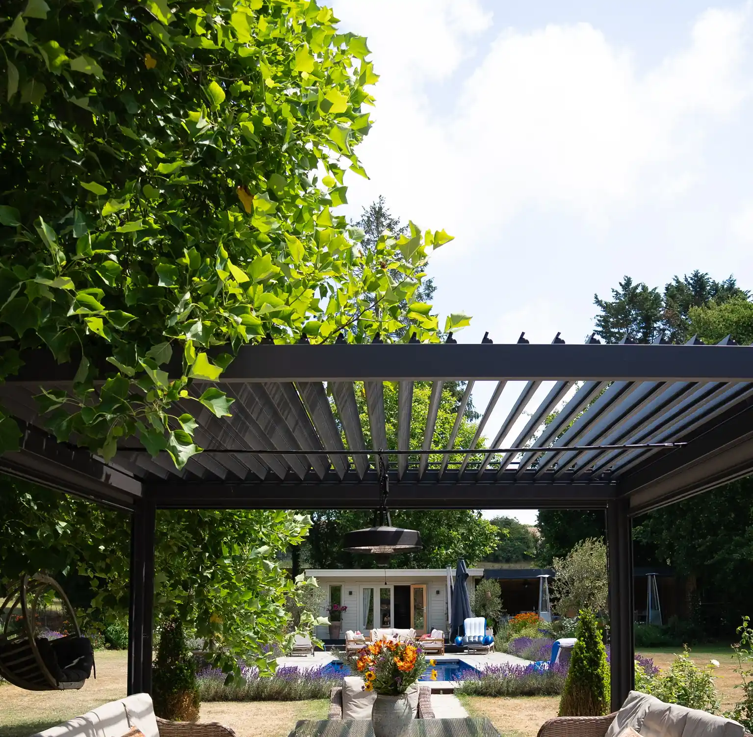 Louvred aluminium pergola over rattan seating, the blades open to the sky and the garden visible beyond