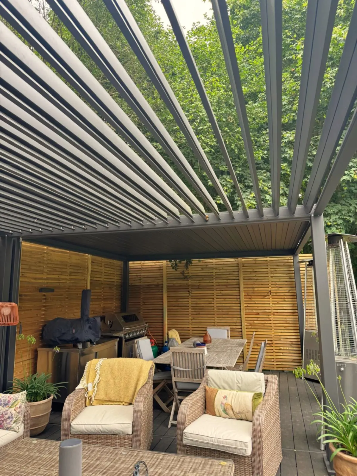 Looking up into anthracite aluminium louvre blades from below, seating and an outdoor kitchen visible underneath