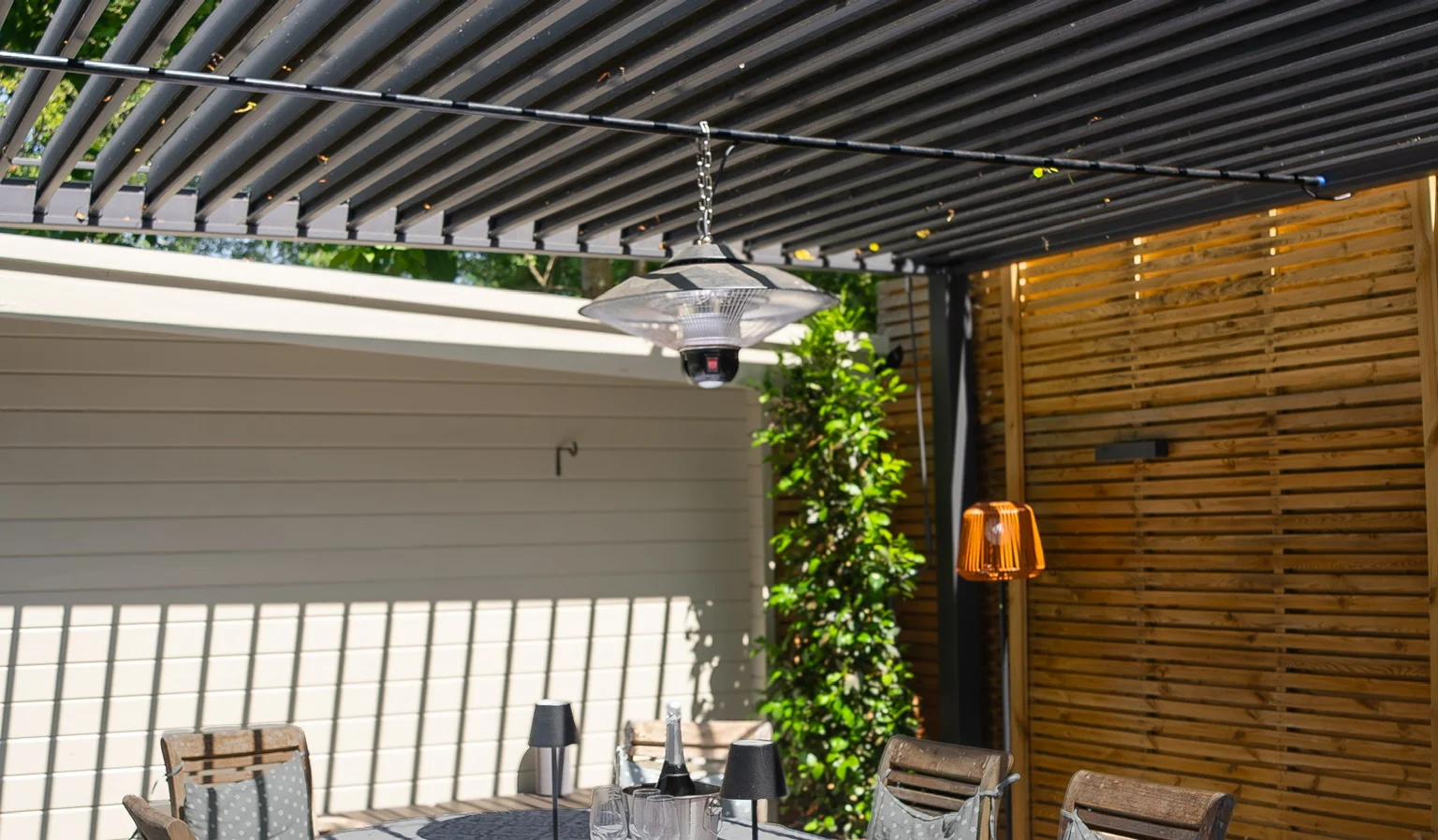 Open aluminium louvre blades above a dining table, throwing striped shadows across the wall and the tablecloth