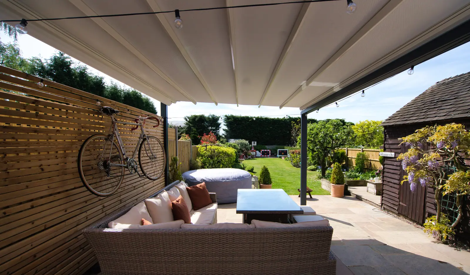 Retractable white fabric canopy extended over a paved terrace with rattan seating, the folded ribs of the canvas visible from underneath