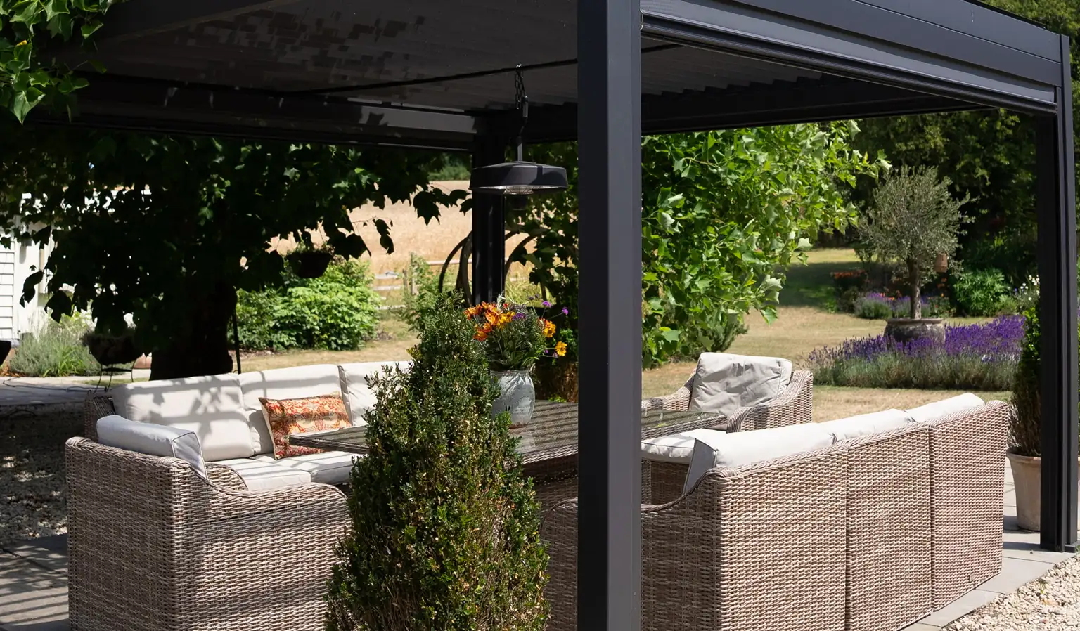 Aluminium pergola over corner sofas on a paved terrace, lavender borders and open lawn behind
