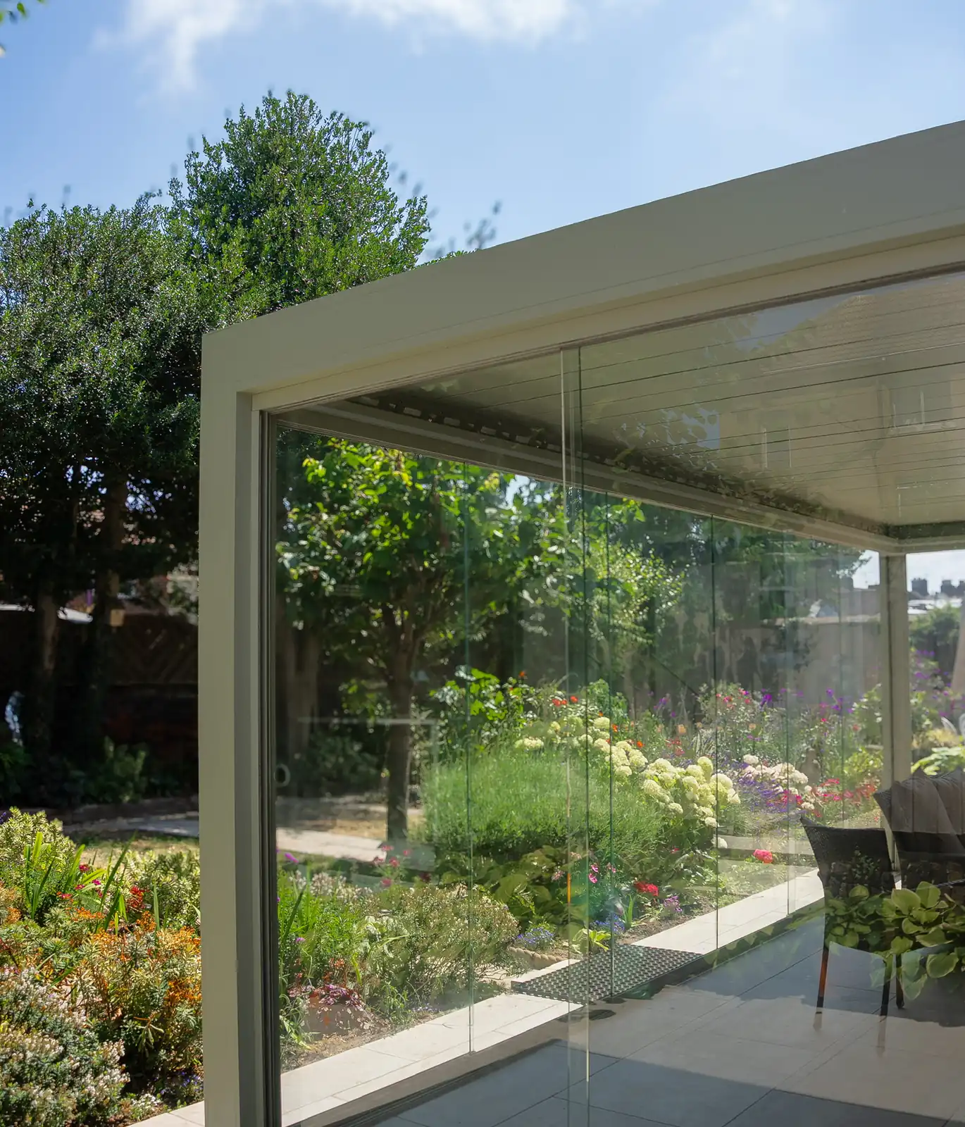 Frameless glass corner of an aluminium veranda opening onto a planted border and paved terrace