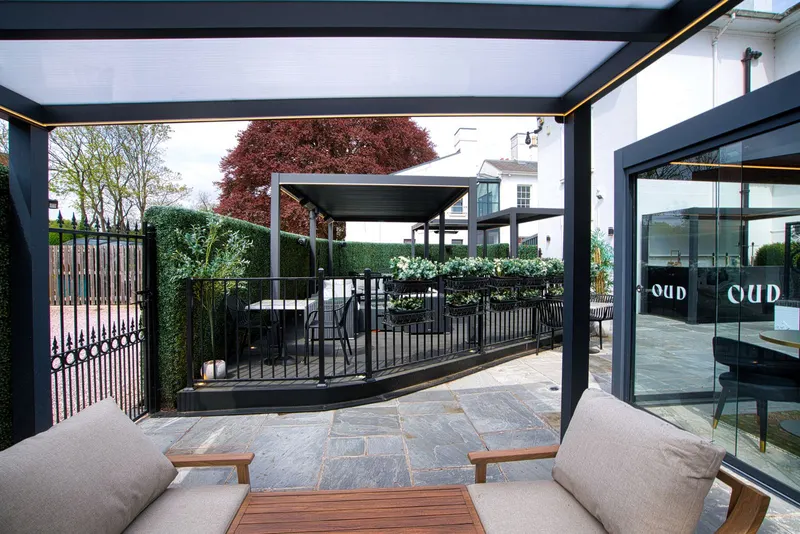 View out from under a Deponti Bosco veranda towards a restaurant terrace and garden gates