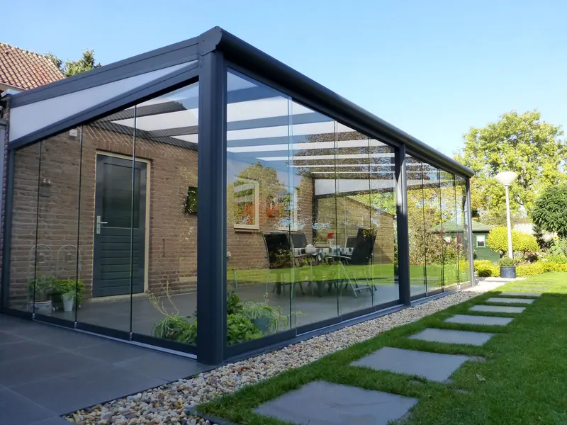 Deponti Fiano glass sliding walls enclosing a veranda beside a brick house and lawn path