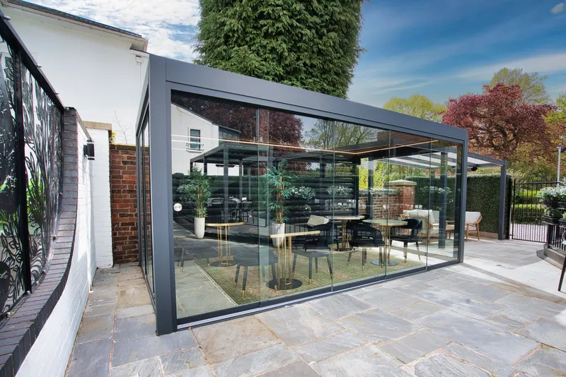 Deponti Fiano glass sliding walls enclosing a louvred pergola dining area on a stone terrace