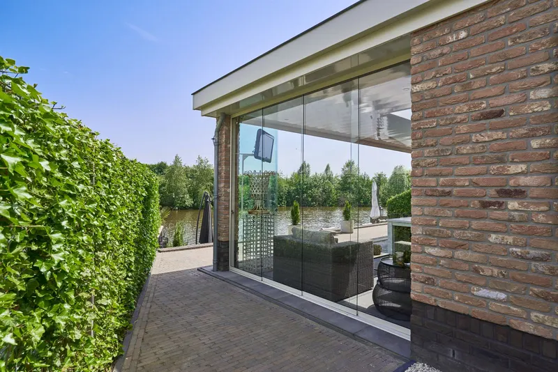 Deponti Fiano glass sliding walls under a veranda roof next to a brick wall and hedge