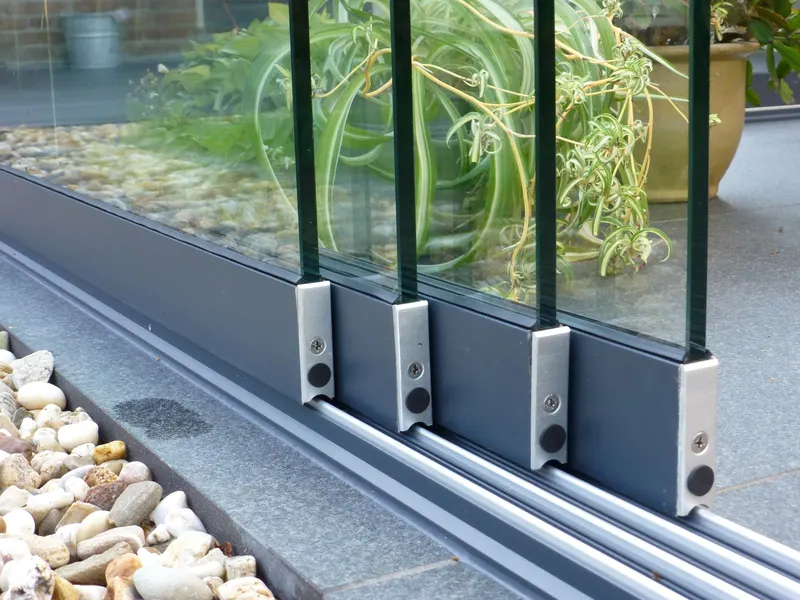 Close view of Deponti Fiano glass panels running in their floor track beside pebbles