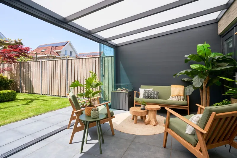 Deponti Giallo veranda with glass sliding walls sheltering garden chairs, sofa and plants