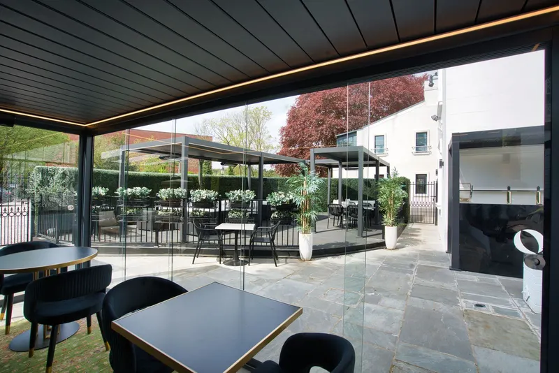 Deponti Pinela louvred roof with glass walls over dining tables on a stone terrace