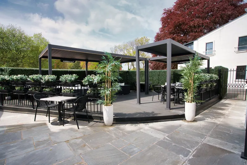 Deponti Pinela pergolas over café tables on a stone terrace with potted bamboo