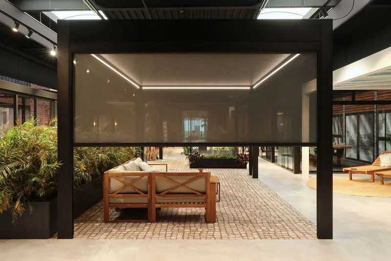 Deponti Screen half lowered on a black pergola above a teak sofa in a showroom