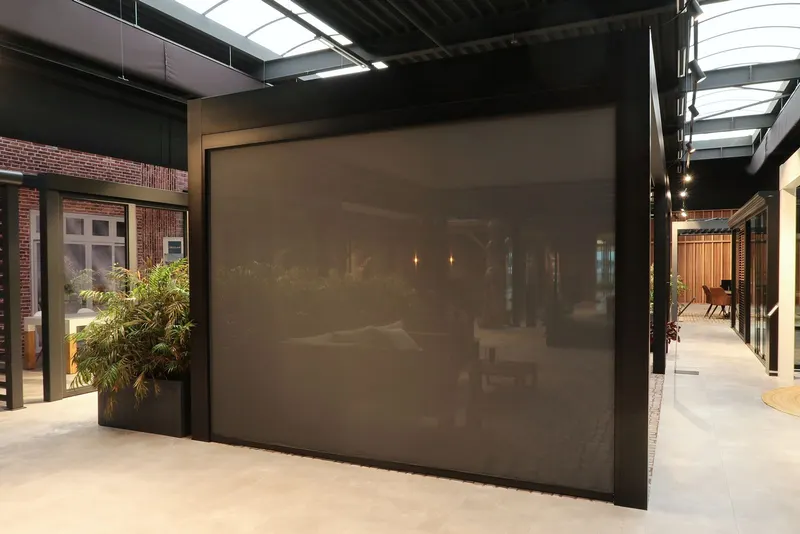 Deponti Screen fully lowered along the side of a black pergola in an indoor showroom