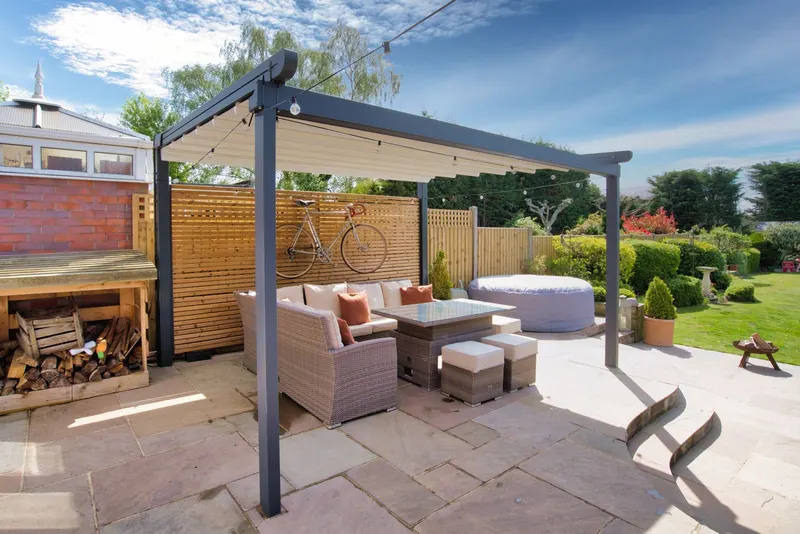 Deponti Verdeca pergola with anthracite frame over patio seating beside a timber fence