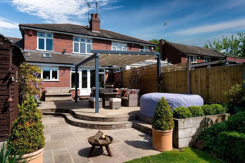 Deponti Verdeca pergola on a stone patio seen from the lawn of a brick house