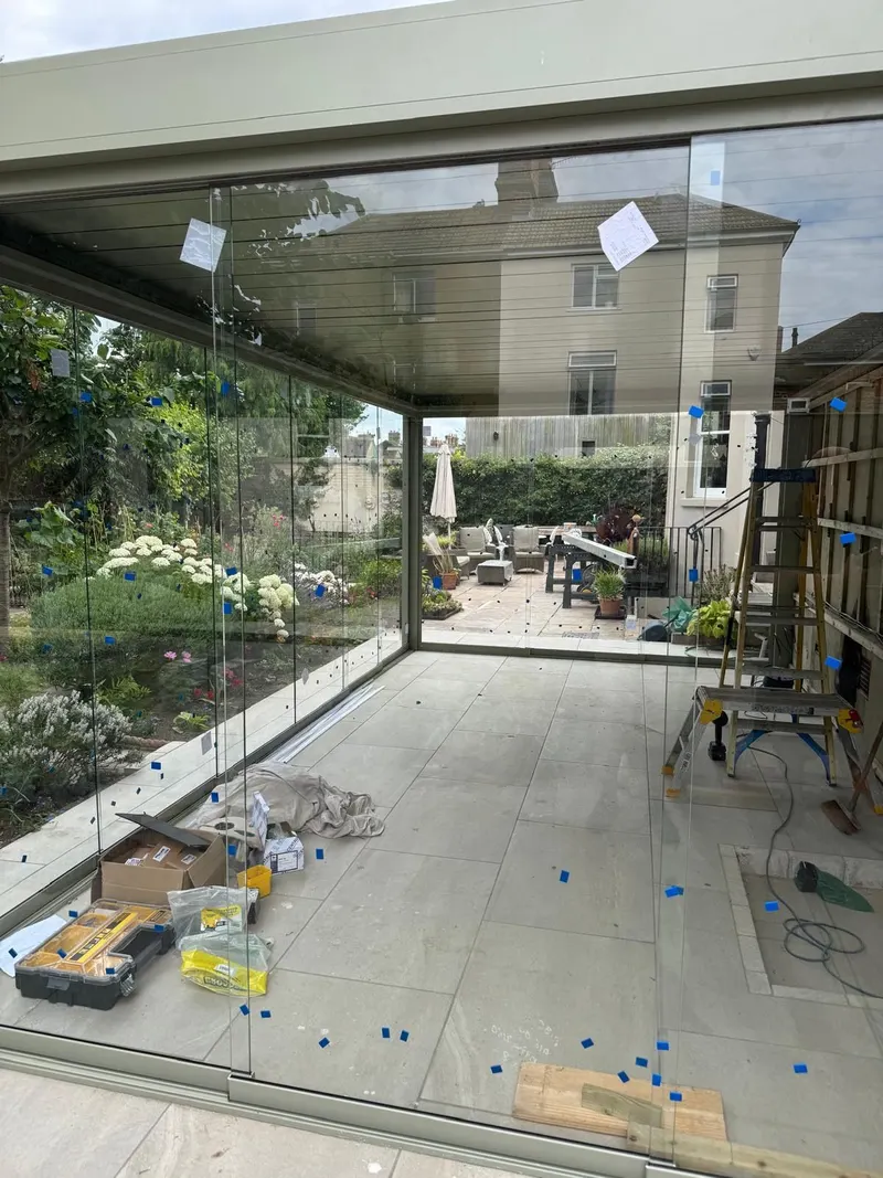 Inside a sage green Morvelle pergola looking out through frameless glass walls to the garden