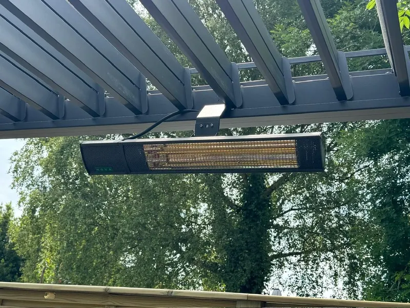 Slim black infrared heater mounted beneath the open louvre blades of an Eden Titan pergola