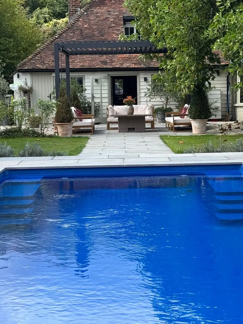 Eden Titan pergola with lounge seating in front of a weatherboard cottage, swimming pool in the foreground