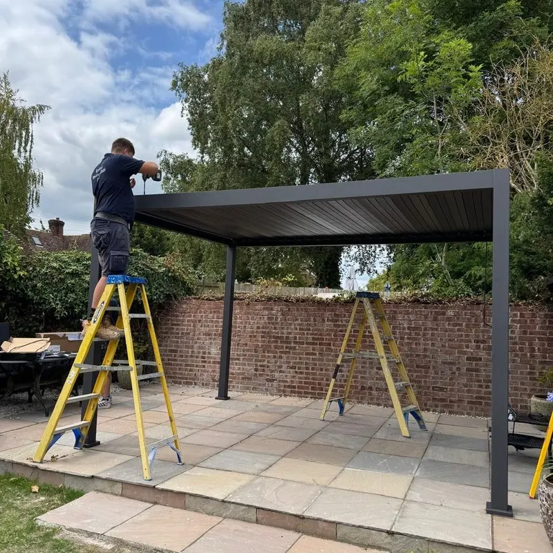 Eden Titan pergola frame and roof going up on a sandstone patio beside an old brick wall