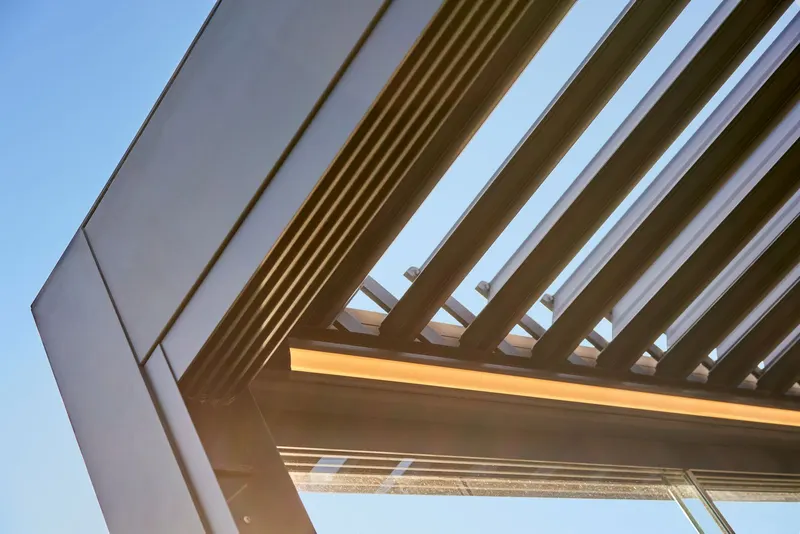 Looking up through open Pinela Deluxe aluminium panels at blue sky, with the LED strip lit along the frame